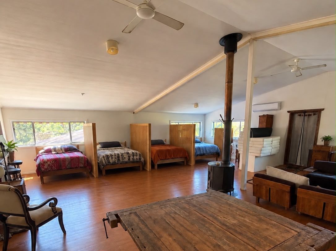 Dorm beds along the wall of the camp house — timber floor, wood stove, a long table