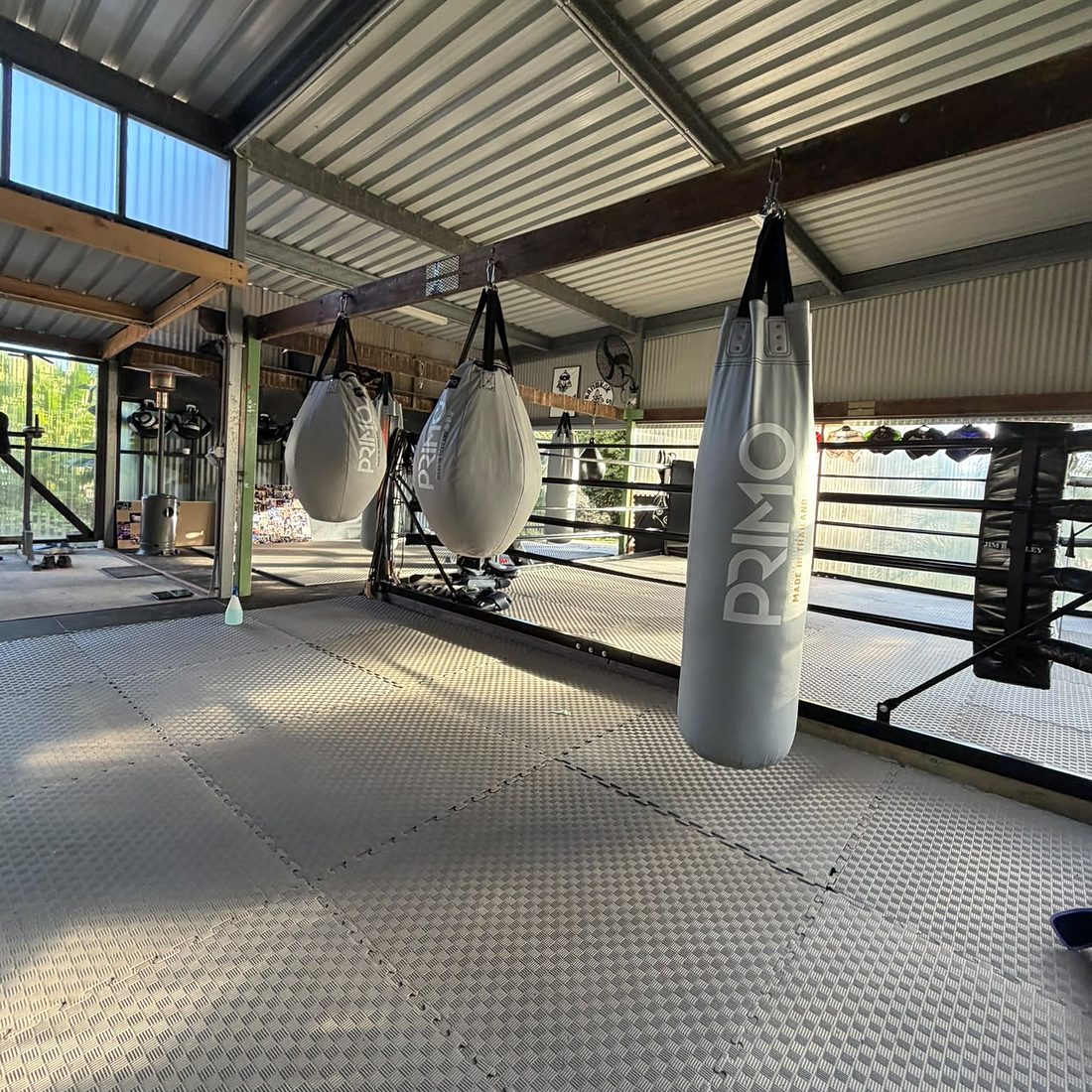 Heavy bags hanging in the training shed, with the ring behind them